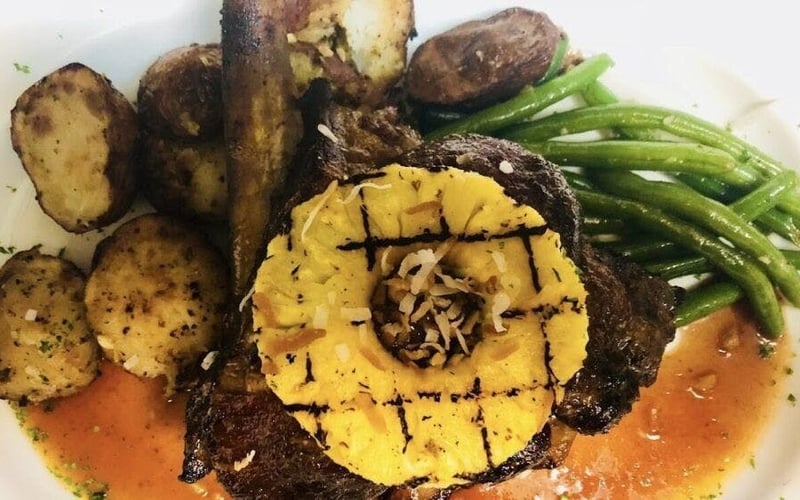 Grilled steak topped with pineapple ring, roasted potatoes and green beans